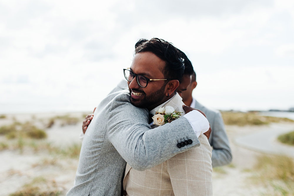 groom hugging a friend at the beach in Copenhagen