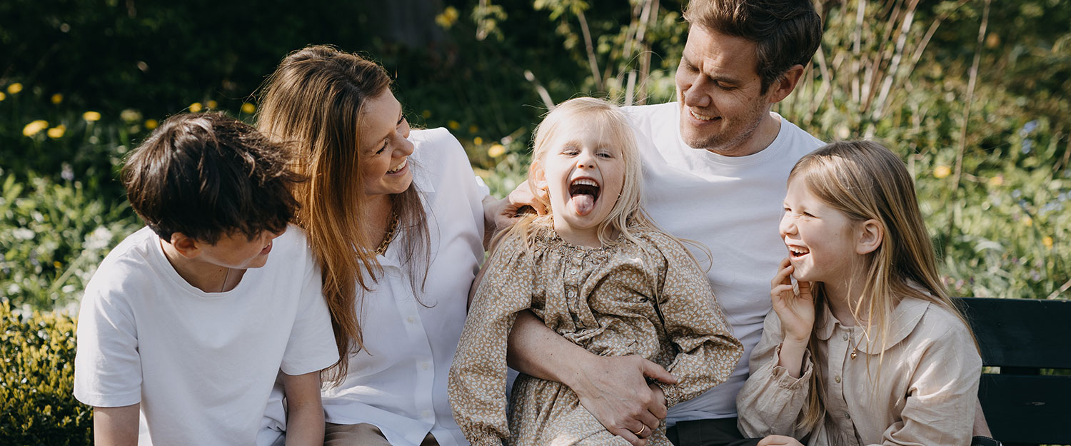 Family photography Copenhagen: A happy family of five posing together in Frederiksberg Have, with the parents embracing their children