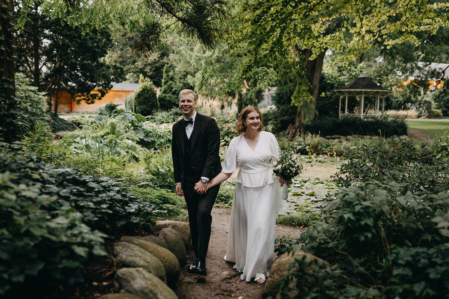 Bride and groom smiling as they stroll hand in hand through Frederiksberg Have's enchanting gardens