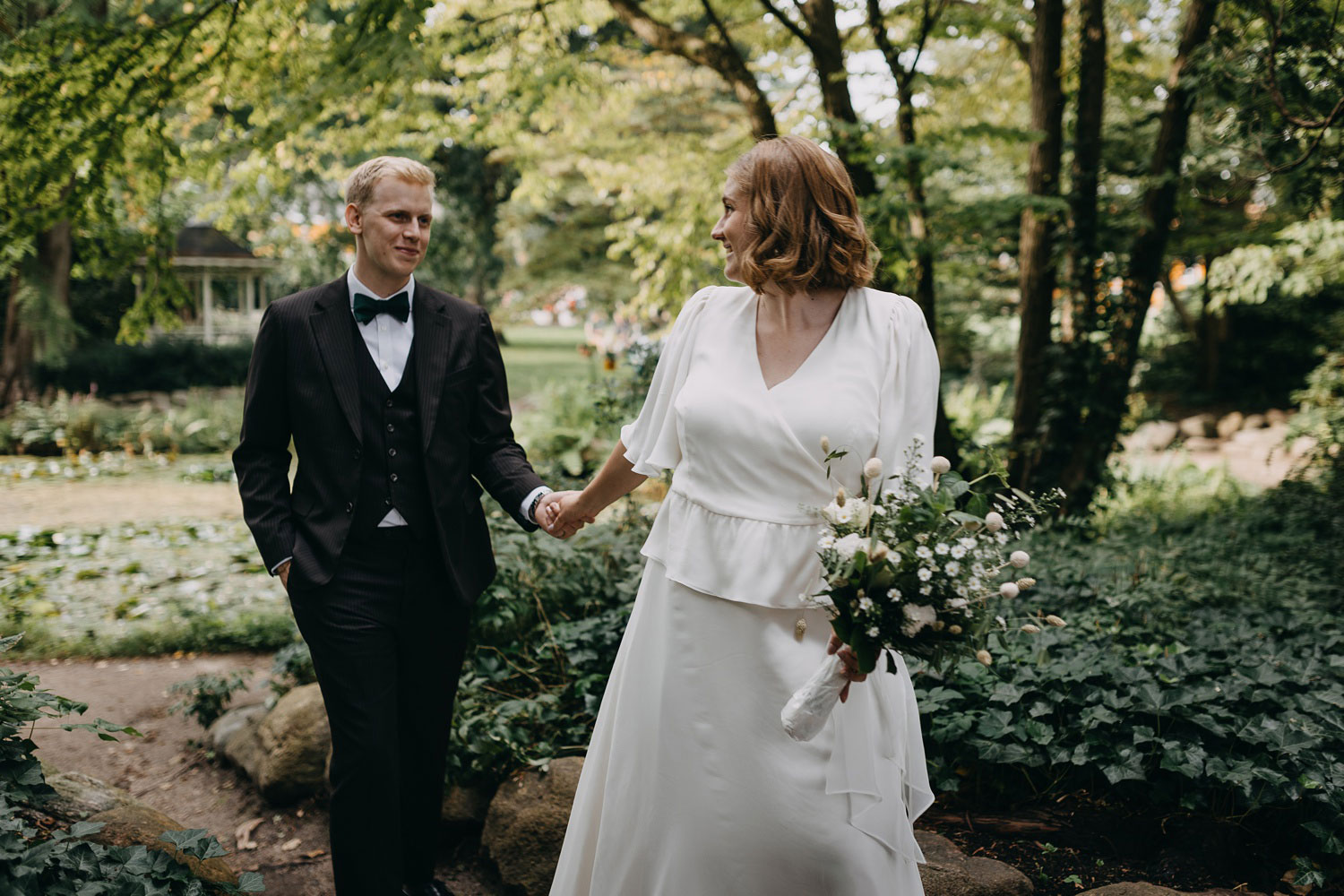 Bride and groom smiling as they stroll hand in hand through Frederiksberg Have's enchanting gardens