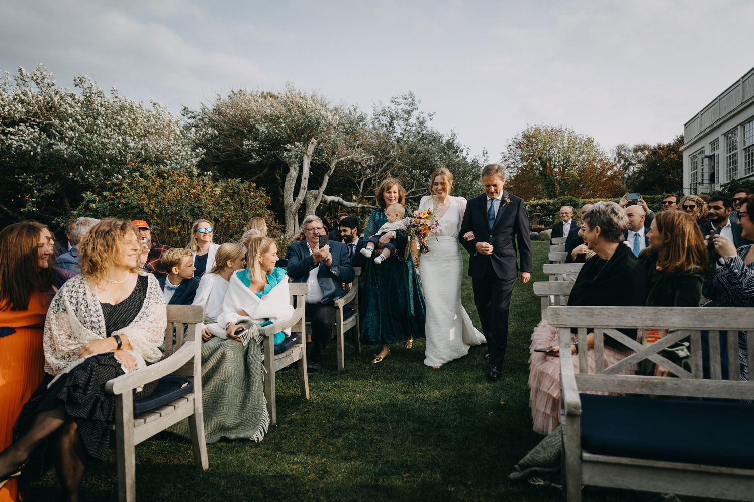 the bride, flanked by her parents and holding her precious baby, makes her way down the aisle at Helenekilde Badehotel