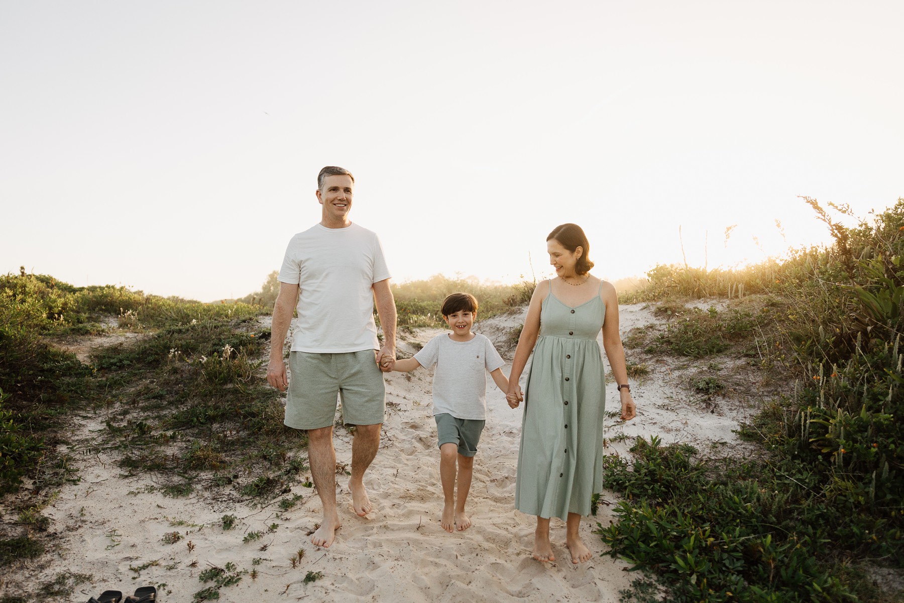 Family walking barefoot through sand dunes during summer photo session at Campeche Beach in Florianópolis, Brazil
