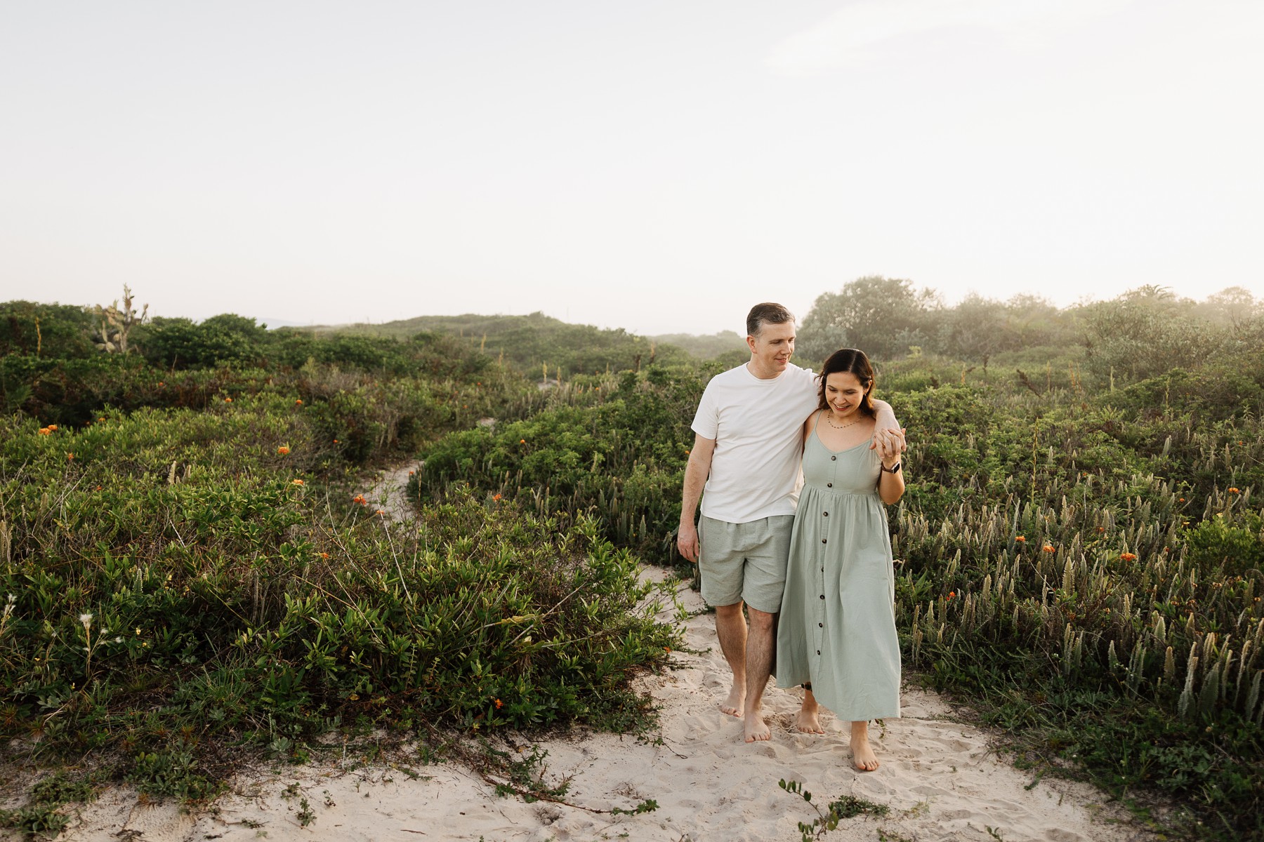 couple walking barefoot through sand dunes during summer photo session at Campeche Beach in Florianópolis, Brazil