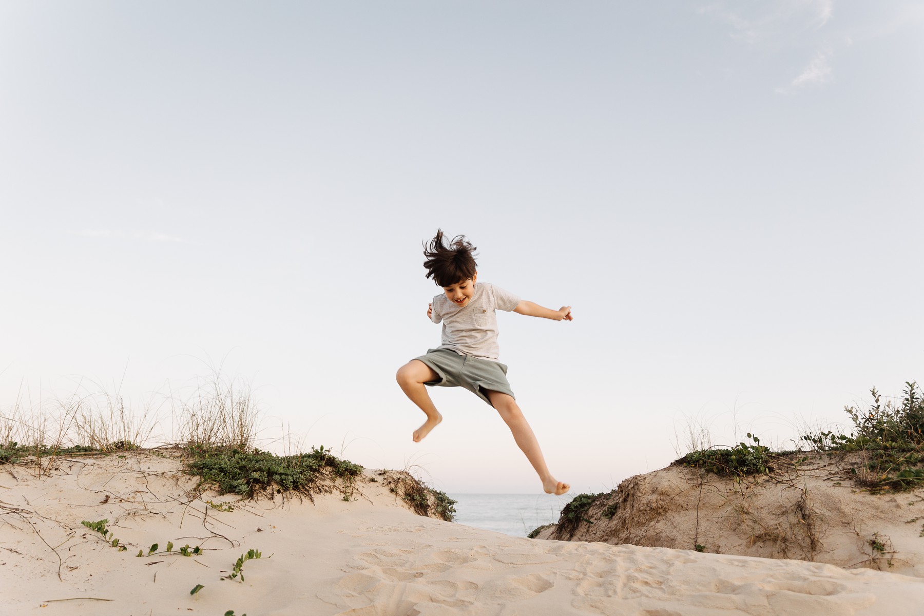 little boy jumping in the dunes during relaxed family photo session by the beach in Brazil